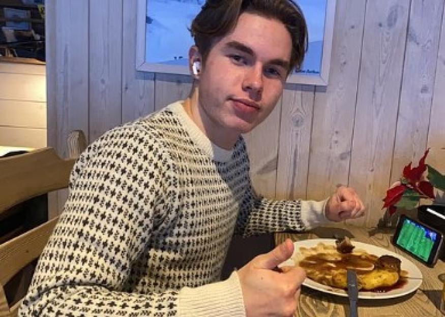 Johannes Natland, a Norwegian teenager, wearing a patterned sweater, gives a thumbs-up while sitting at a table with a plate of food.