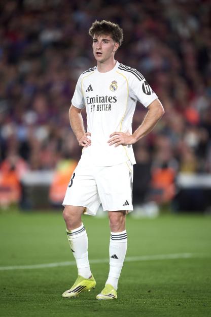 A Real Madrid CF player in a white uniform stands on the field during the LaLiga EA Sports match against FC Barcelona.