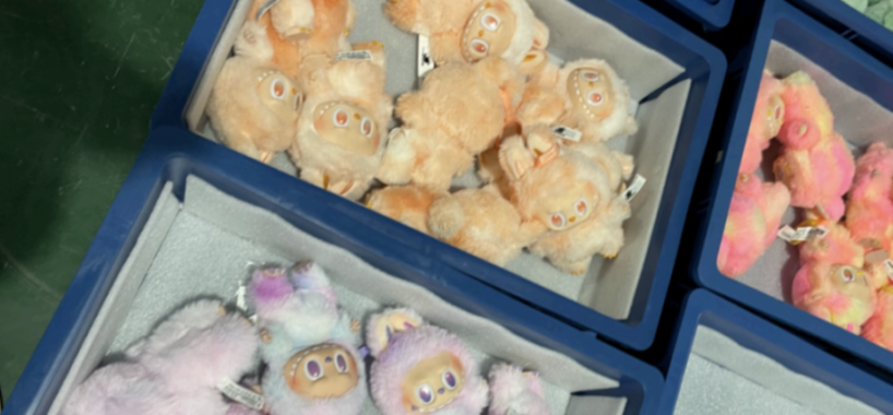 Three bins of Labubu plush toys, varying in color from light orange to pink and purple.