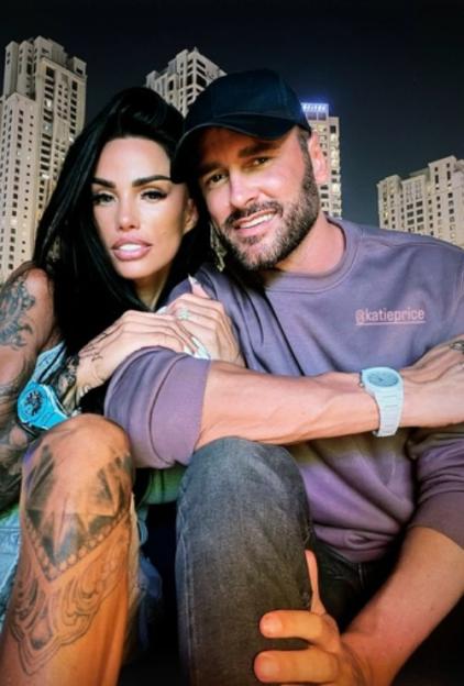Katie Price and Carl Woods posing for a selfie with city buildings in the background.