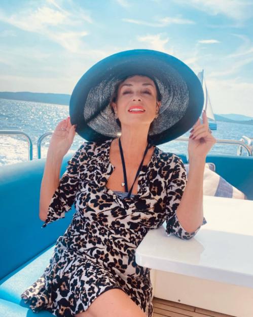 Woman in a leopard print dress and sun hat on a boat.