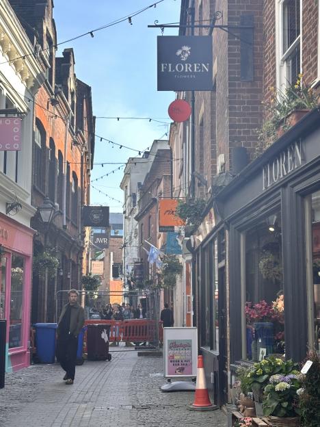A narrow street in Exeter, lined with brick buildings housing shops like Floren Flowers and Chococo.