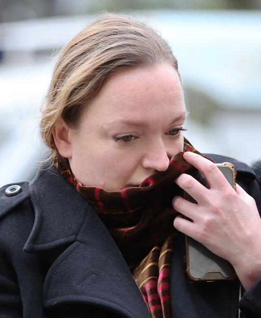 Catriona Londie Gourlay covering her face with a brown and red striped scarf, holding a phone.