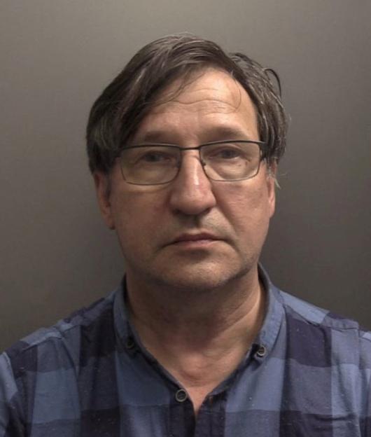 Mugshot of Russian national Vladimir Motin wearing glasses and a blue plaid shirt.