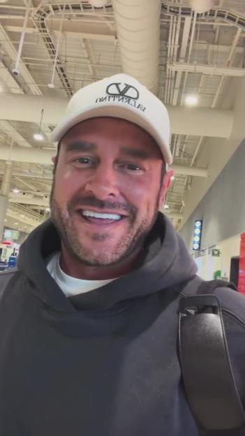 Lee Andrews smiling while wearing a white cap and black hoodie.