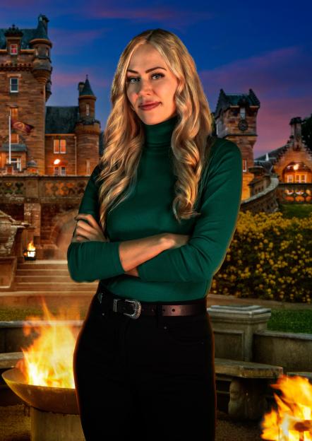 Ellie, a 33-year-old psychologist from London, stands with arms crossed in front of a castle and a fire pit.