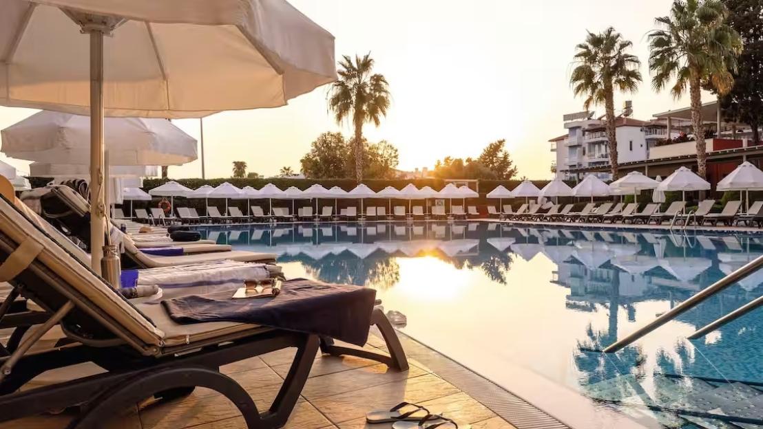 A resort swimming pool with many lounge chairs and white umbrellas, reflecting the golden sunset.