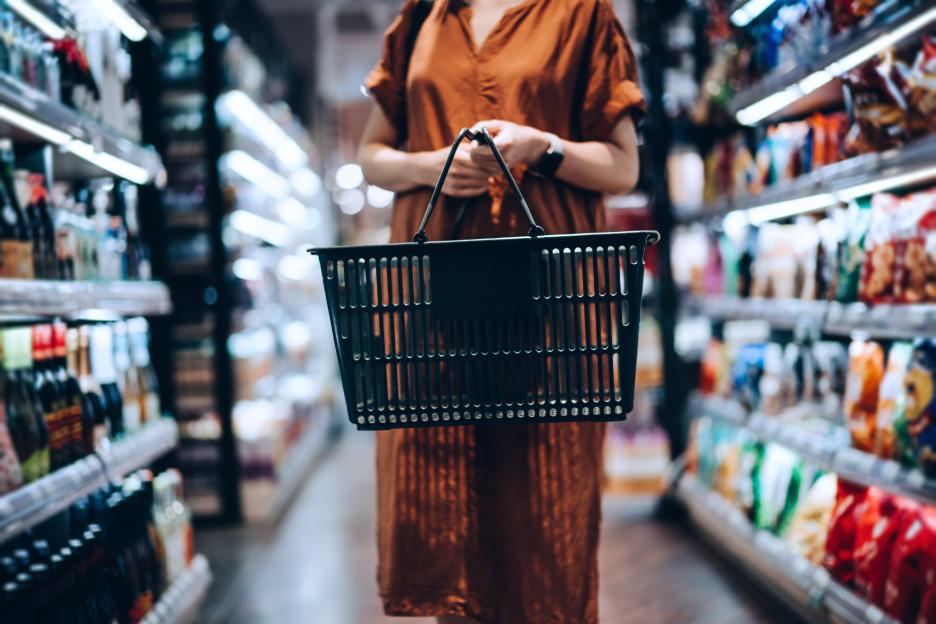 Cropped shot of young woman carrying a shopping basket, grocery shopping for daily necessities in supermarket.