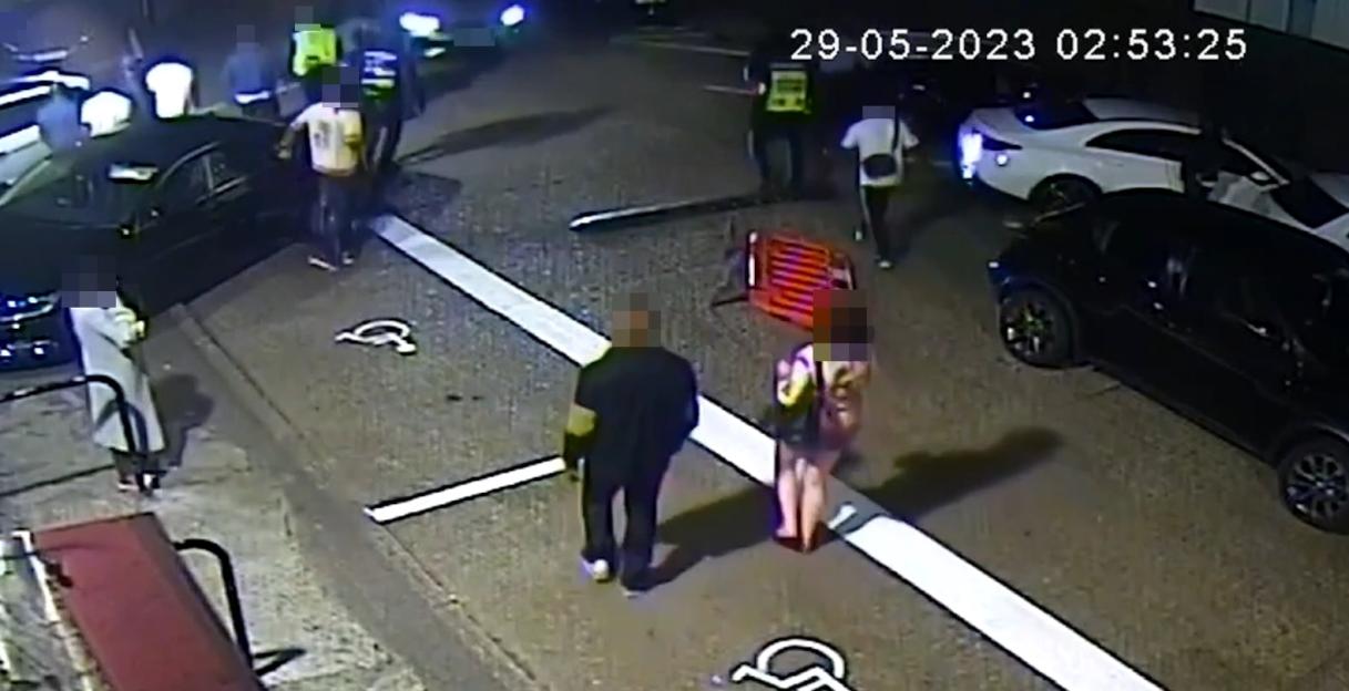 CCTV footage of people gathered around cars at night on a street.
