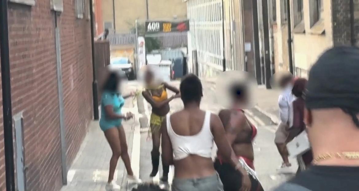 Several women fighting in a street alleyway.