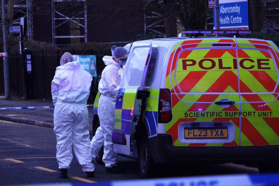 Police officers in forensic suits by a police Scientific Support Unit van.