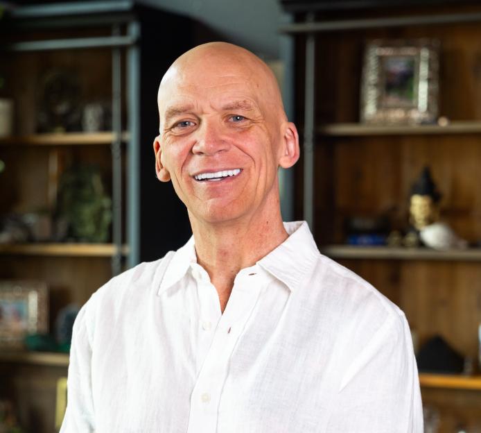 Headshot of a smiling bald man in a white linen shirt.