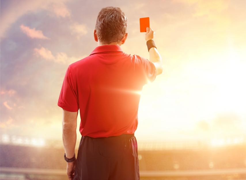 A referee displays a red card with his back to the viewer.