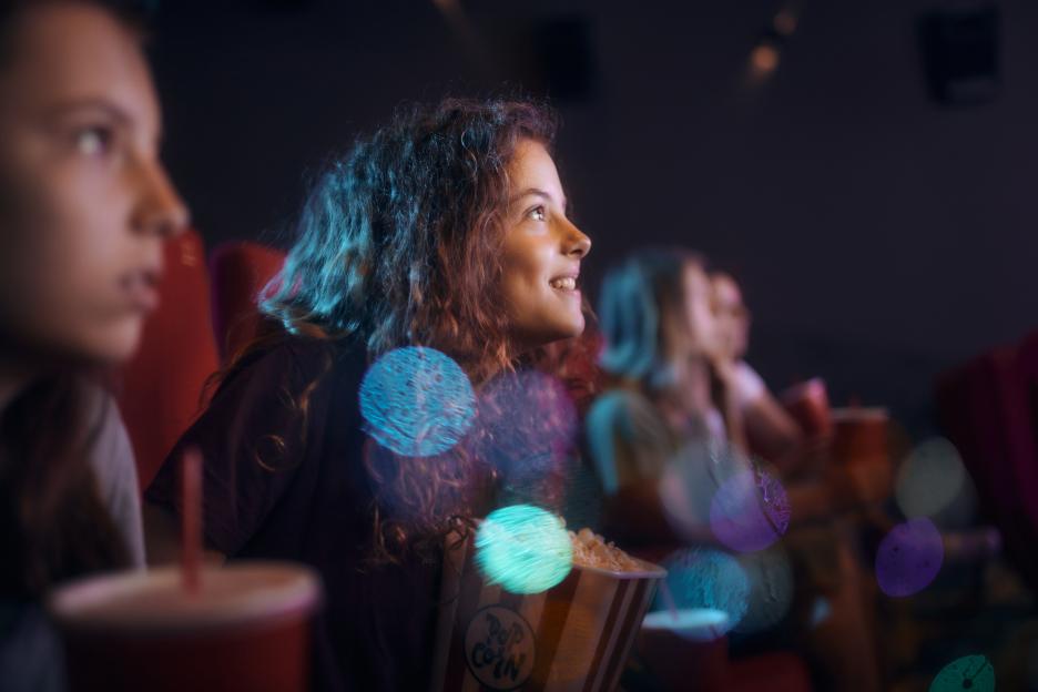 Happy little girl enjoying in movie projection at theatre.