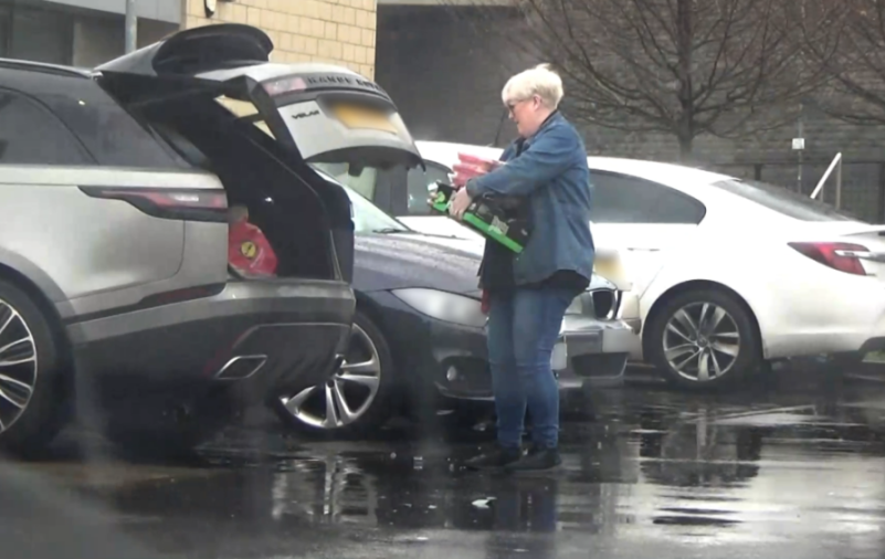 A person carrying multiple items from their car in a parking lot.