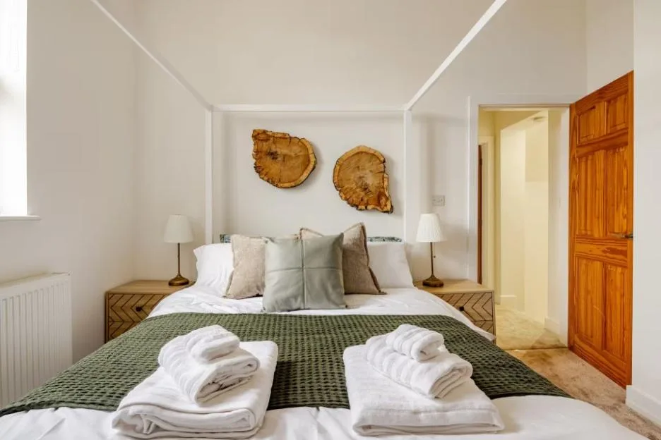 Brightly lit white bedroom with a double bed, decorated with two large tree-slice wall hangings, and an open wooden door leading to another room.