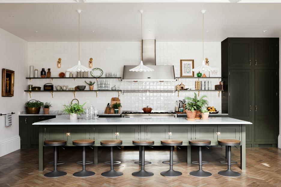 Spacious kitchen with a green island and cabinets, white tiled walls, and herringbone wood floor.