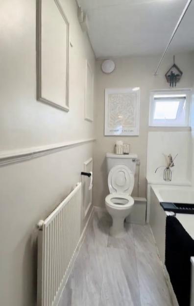 A newly renovated bathroom with light grey walls, a toilet, a bathtub, and a radiator.