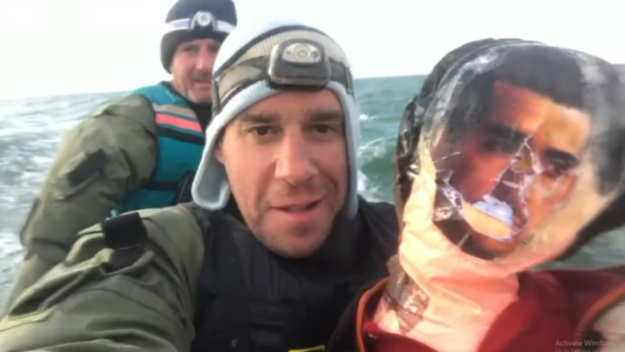 A man in a boat with a headlamp on his hat and another man behind him, with a photo of a man on a plastic bottle next to them.