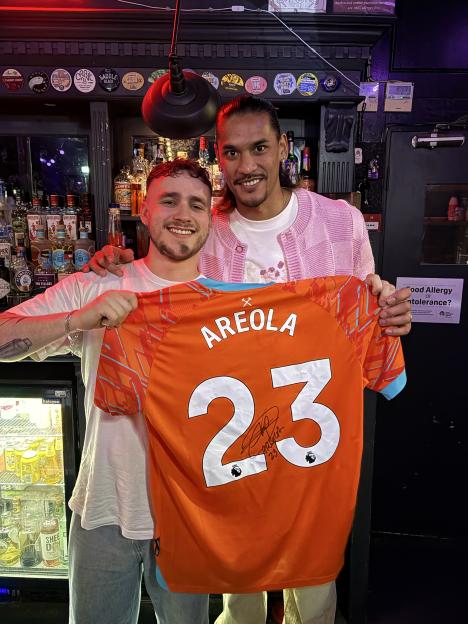 West Ham United goalkeeper Alphonse Areola holding his signed "AREOLA 23" football jersey with Archie, the pub manager at The Star of Bethnal Green.