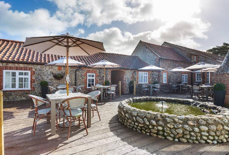 Outdoor seating area at Blakeney Manor with umbrellas, tables, and a stone fountain.