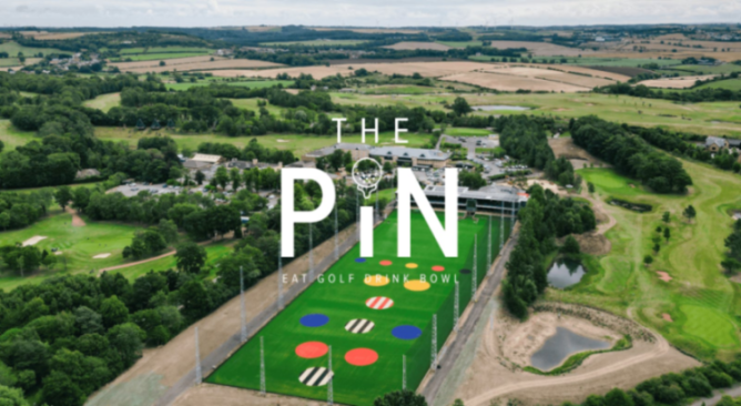 Aerial view of "The Pin" golf range with colorful targets, part of a larger complex surrounded by a golf course and countryside.