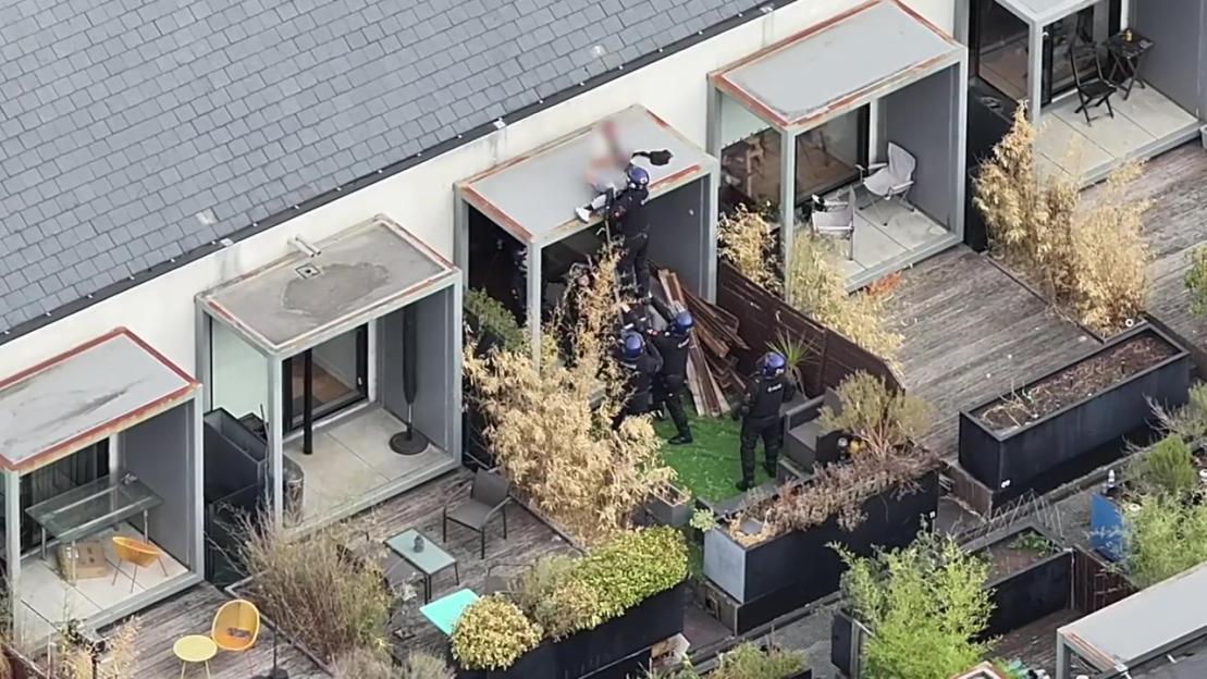 Police officers arresting a man on a rooftop balcony.