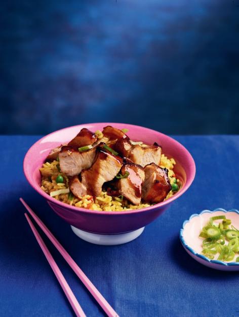 A pink bowl of rice and glazed pork with green onions and pink chopsticks.