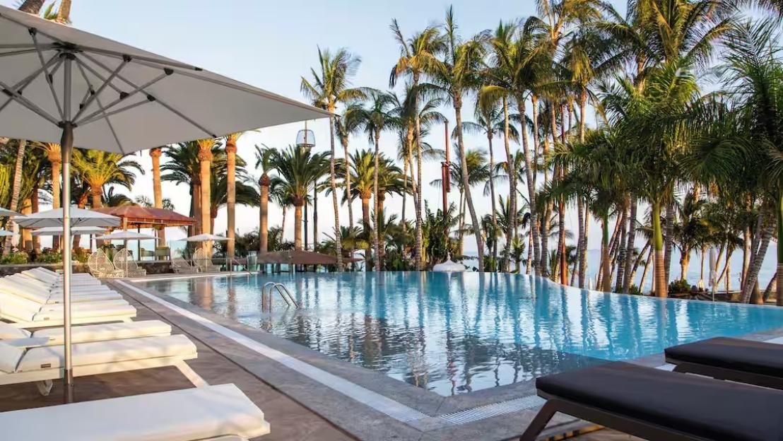Infinity pool with lounge chairs and palm trees at a resort.