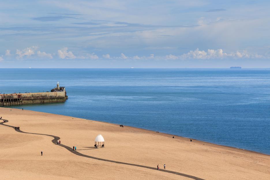 View of Folkestone harbour pier and the Lower Leas, taken from The Leas cliff top. Shipping can be seen in the distance. Kent UK.