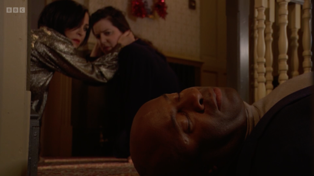 A man lying on the floor, while two women stand behind him looking distressed.