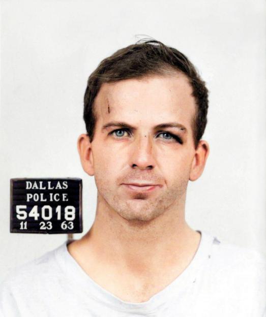 Mugshot of Lee Harvey Oswald with headshots from the front and side, showing injuries to his face, with a "Dallas Police" sign visible in the front shot.