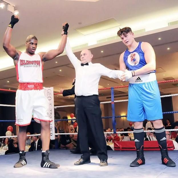 A referee raises a boxer's hand in victory, while the other boxer looks on.