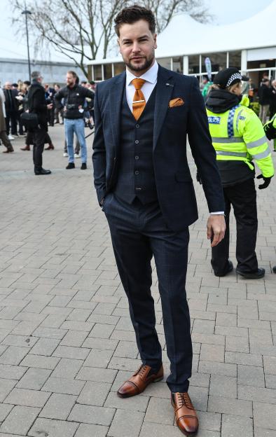 Chris Hughes attending the Cheltenham Festival Gold Cup, wearing a plaid suit with an orange tie and pocket square.