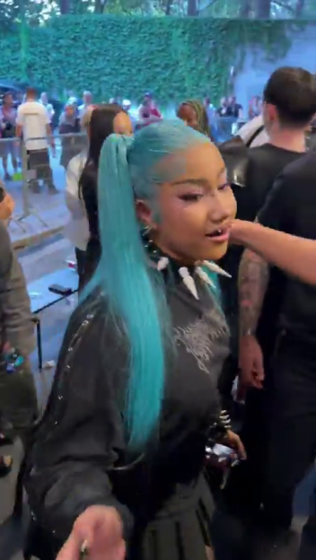 North West in a black outfit, a spiked necklace, and blue hair styled in a high ponytail.