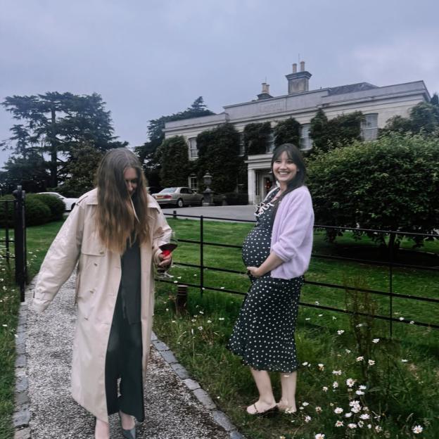 Two women, one pregnant, standing outdoors near a large building.