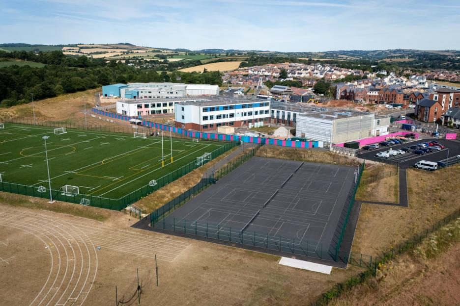 Aerial view of Matford Brook Academy, an unused school in Exeter, with playing fields and distant hills.