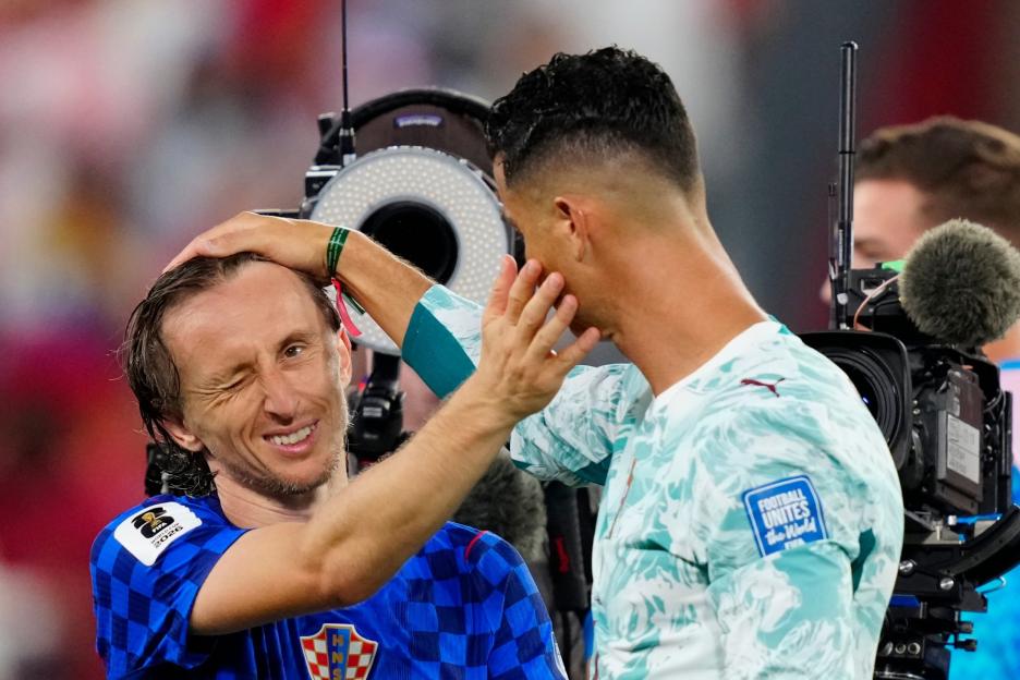 Luka Modric with a wry smile and wink, holding Cristiano Ronaldo's head.