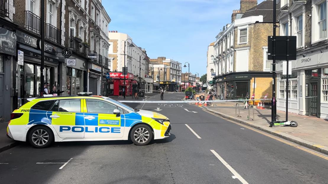 A police car blocks a city street closed off with white and blue tape.