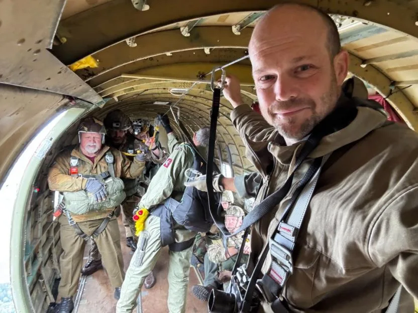 Man in a plane preparing for parachuting with others in the background.