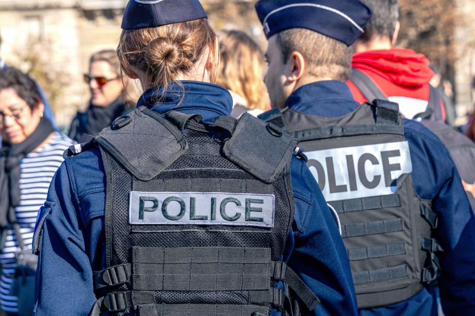 Two policemen, a man and a woman, wearing bulletproof vest with the word police on them.