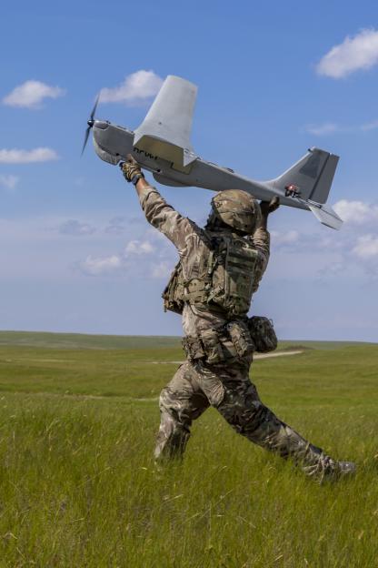 A soldier in camouflage uniform launches a PUMA drone into the sky.