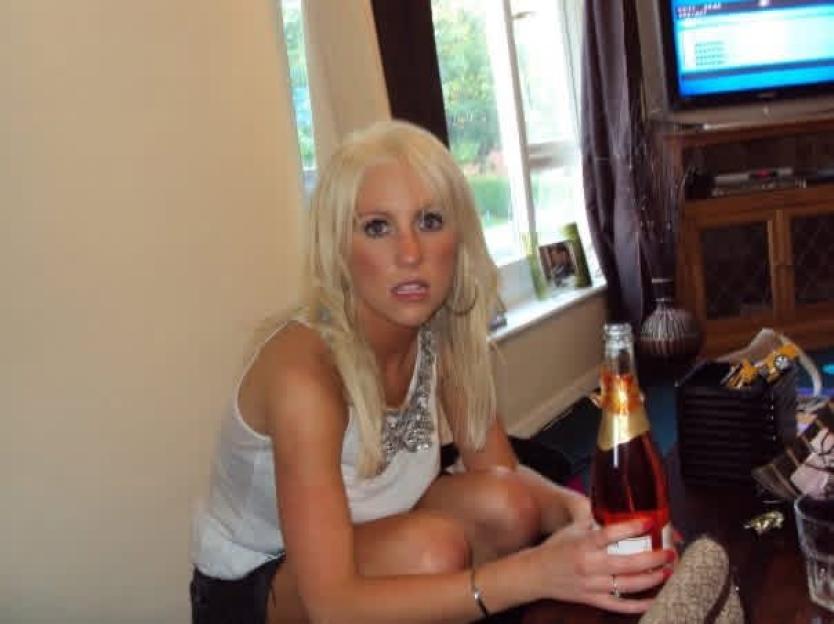 A blonde woman with a necklace is holding a bottle of champagne.