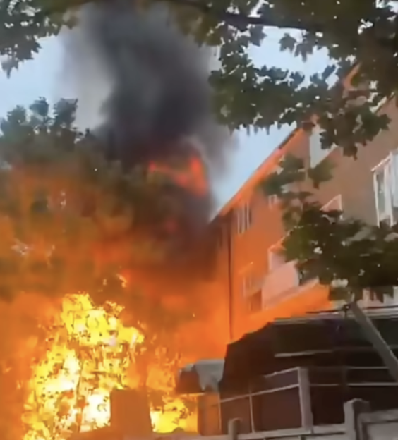 A massive fire erupts from the side of a building, with thick black smoke billowing upwards.