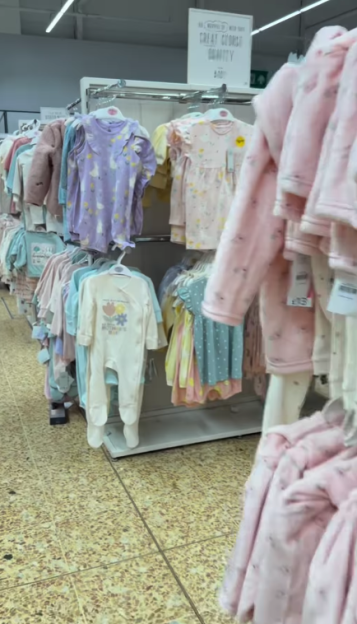 Rows of baby clothes and babygrows displayed on racks in a store aisle.