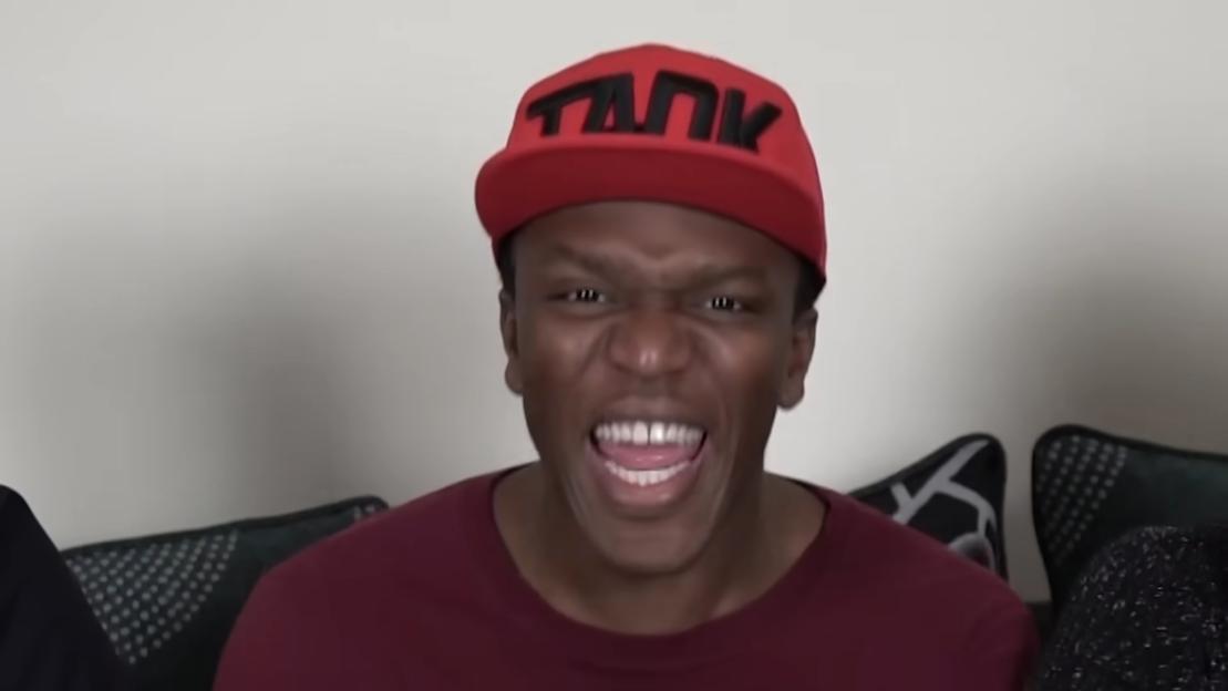 A man with dark skin, wearing a red hat and a red shirt, grins broadly.