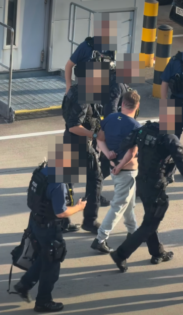 A man in handcuffs being escorted by police officers.