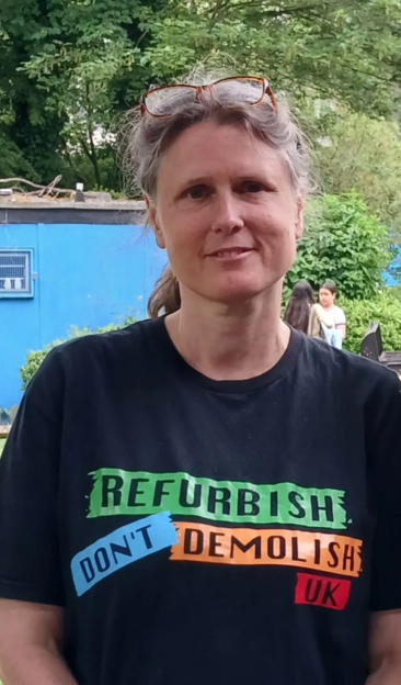 Woman wearing a black t-shirt that says "REFURBISH DON'T DEMOLISH UK" in colorful text.