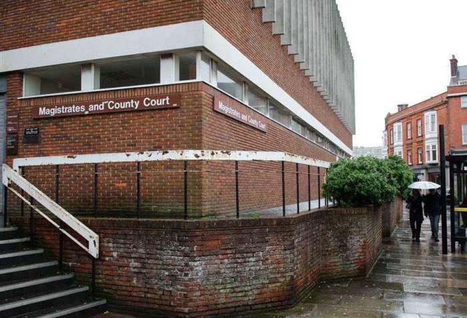 Magistrates' and County Court building, with a brick facade and steps, with two people holding an umbrella walking by.