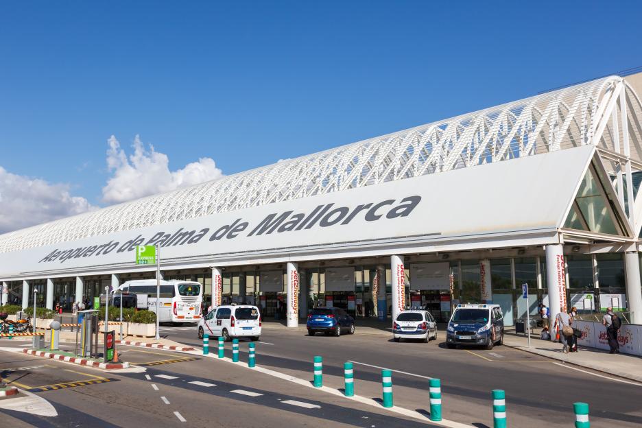 The Palma de Mallorca Airport terminal building in Spain, with cars and a bus outside.